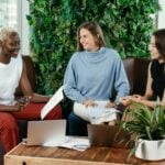 Multiethnic cheerful women talking about agreement at table with laptops