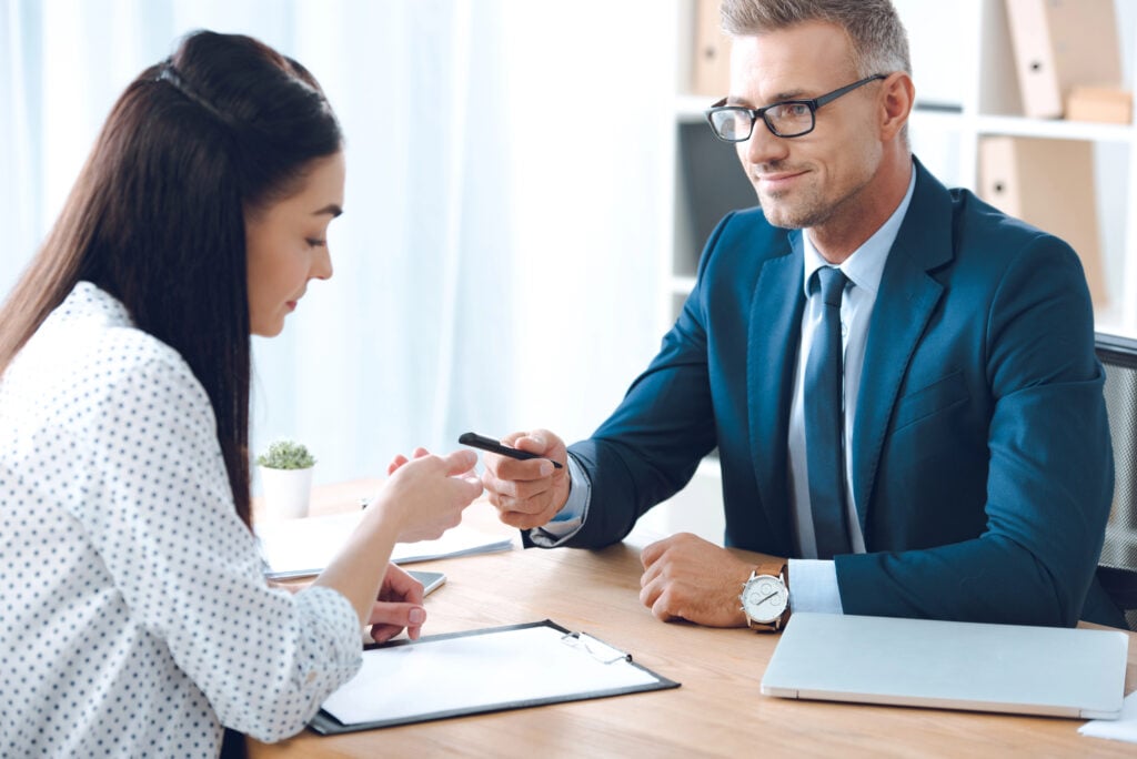 Smiling insurance agent giving pen to female client for signing