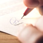 Man writing signature with pen on paper