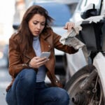 Displeased woman dialing for help after a car accident in the city.