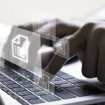 Hand with document icons and typing to laptop computer