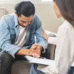 Psychology, depression. Sad asian young man consulting with psychiatrist while patient counseling mental therapy problem with doctor at clinic. Psychologist encouraging with sick mental health person.