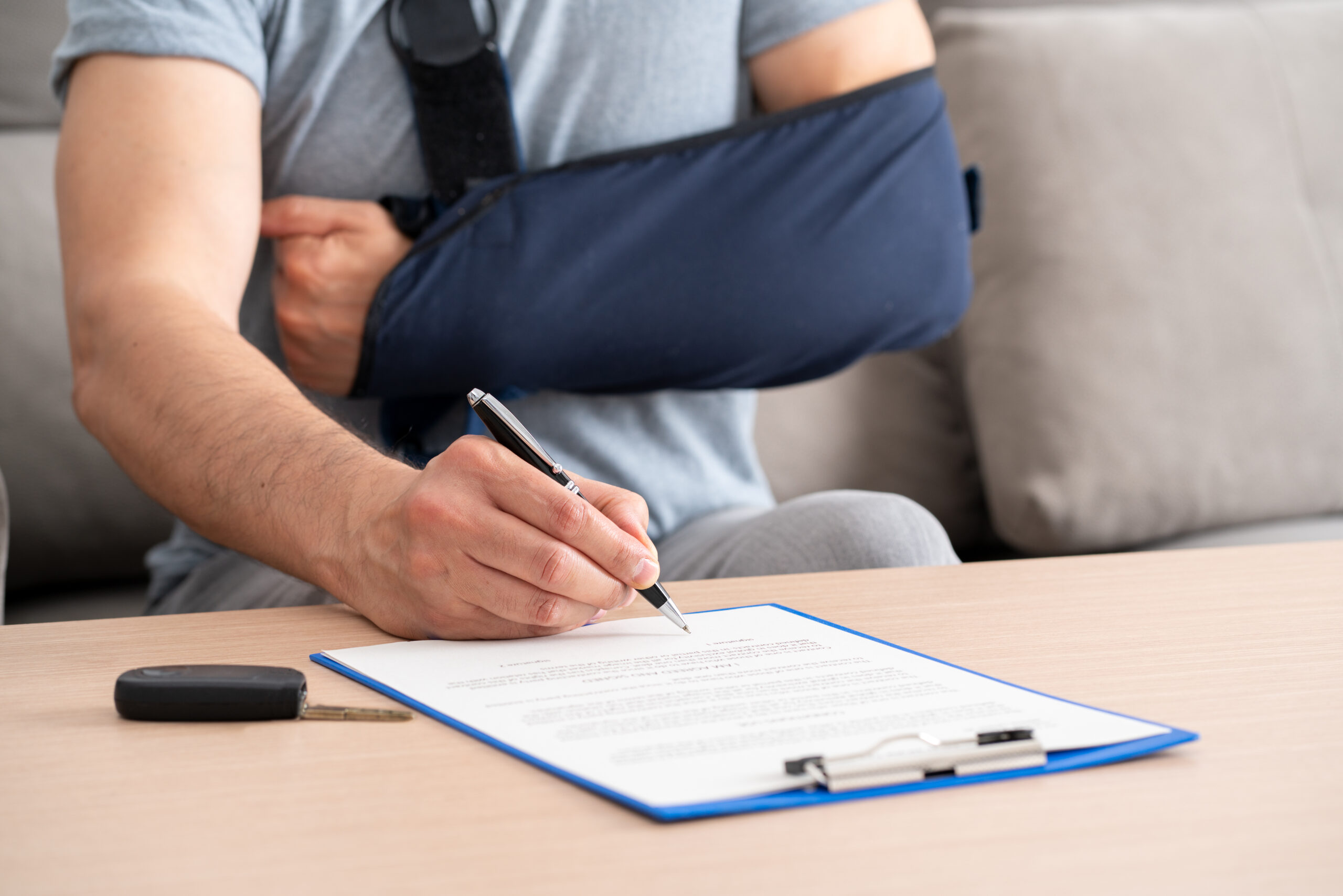 Close up of a man hands with broken arm signing insurance document after car accident at home Close up of a man hands with broken arm signing insurance document after car accident at home
