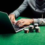 Cropped view of man typing on laptop near poker chips