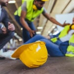 A workplace accident scene showing coworkers aiding a fallen worker