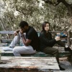 A couple sits back to back on a wooden bench