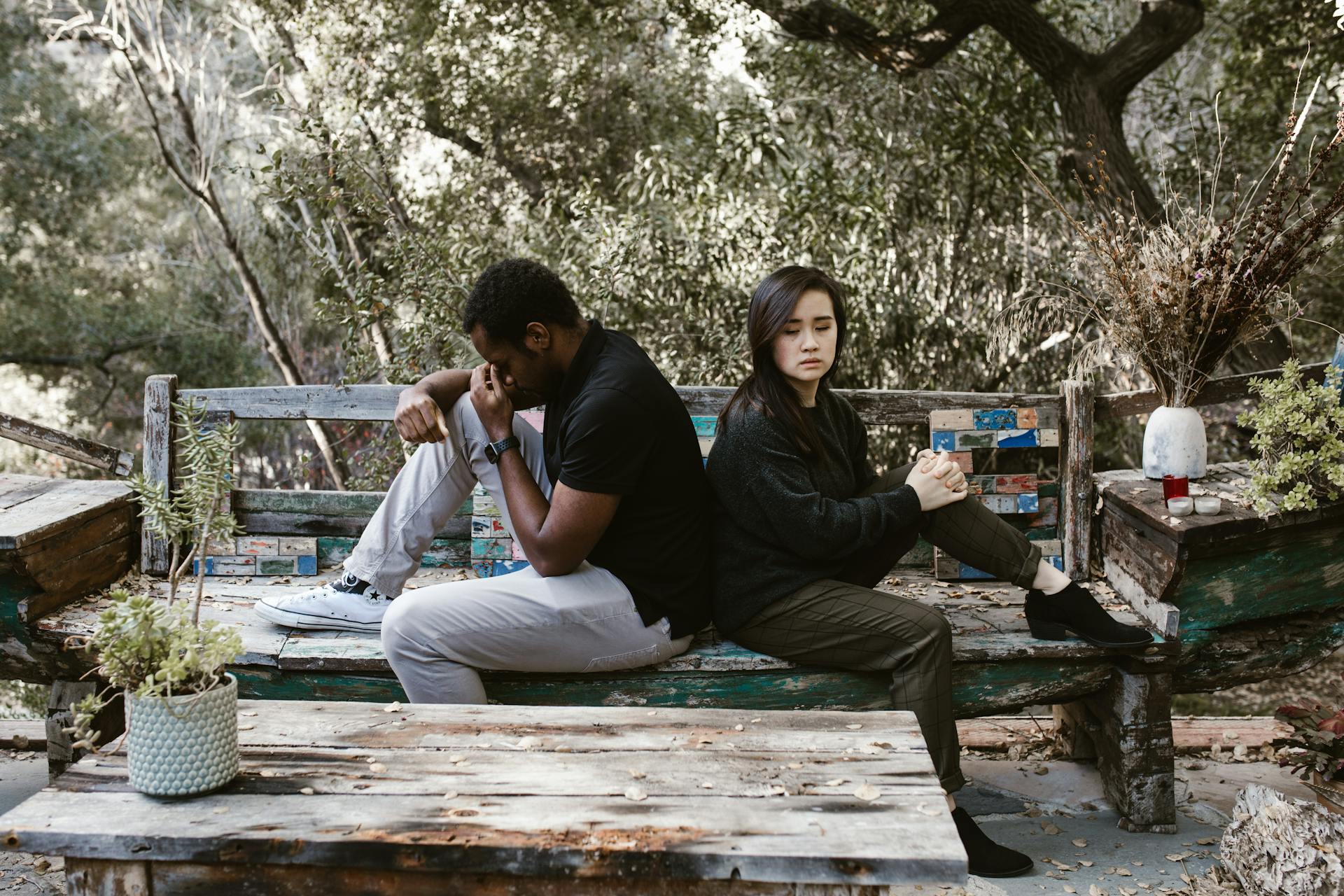 A couple sits back to back on a wooden bench