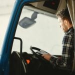 A man sitting in a truck cabin reading a document inside a blue truck