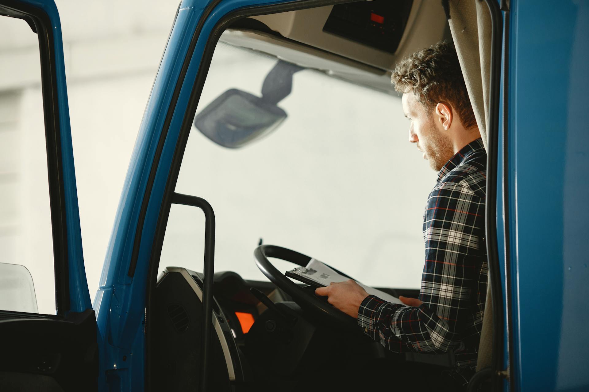 A man sitting in a truck cabin reading a document inside a blue truck