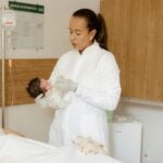 A medical practitioner gently holds a newborn