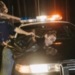 A police officer handcuffing a suspect on a patrol car at night