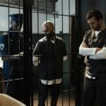 A police officer stands by two prisoners in jail