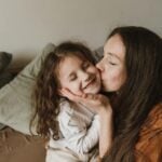 A tender moment of a mother kissing her smiling daughter indoors