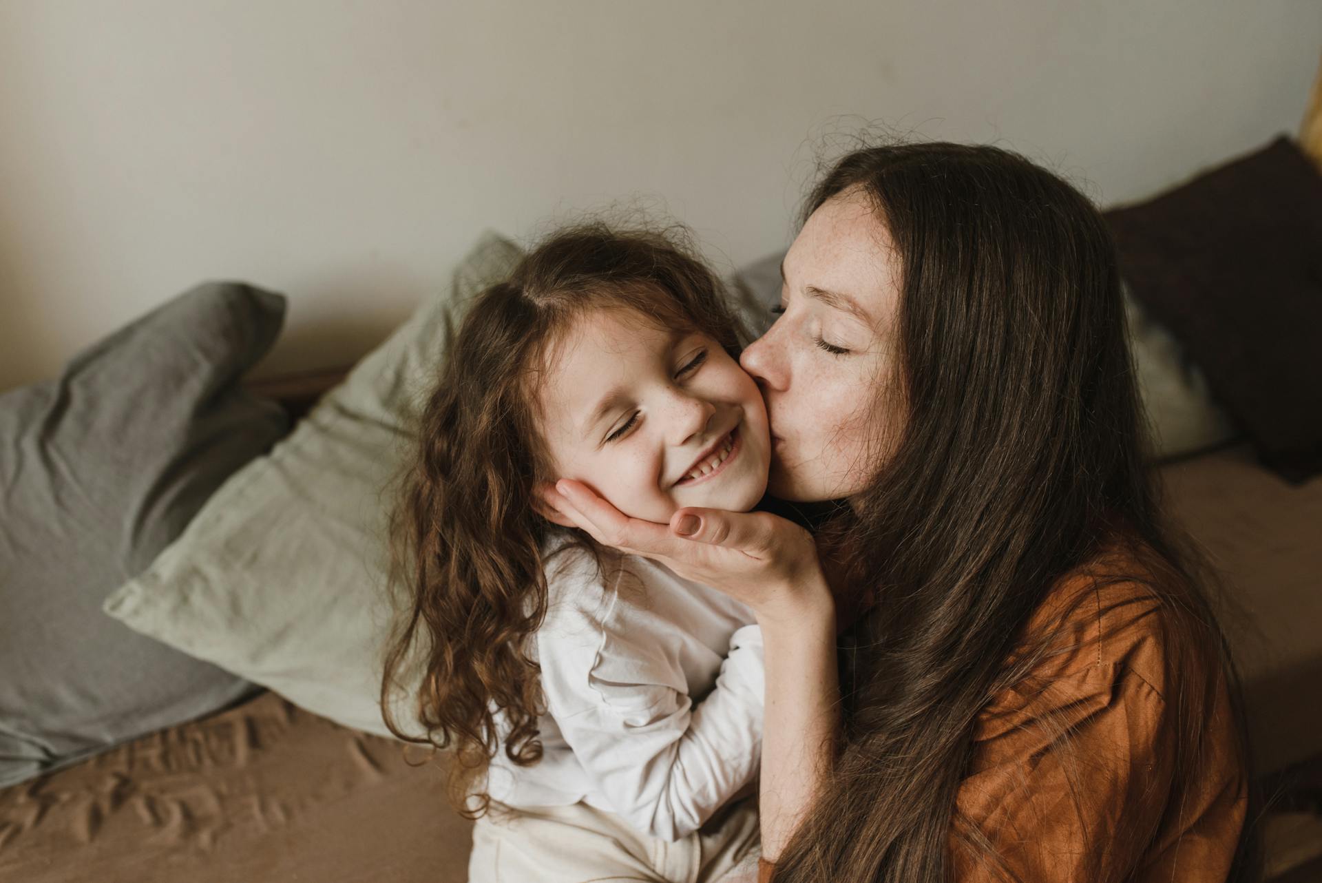 A tender moment of a mother kissing her smiling daughter indoors