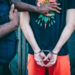 Close-up of a handcuffed person under arrest by a police officer outdoors