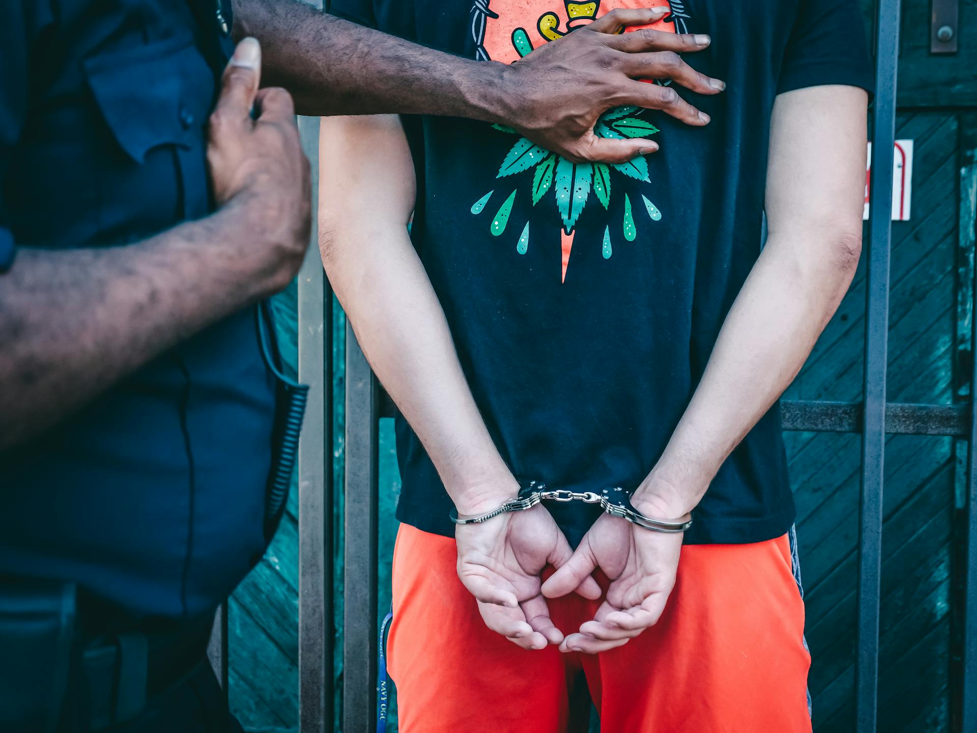 Close-up of a handcuffed person under arrest by a police officer outdoors