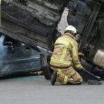 Firefighter in gear assisting at an overturned car crash scene