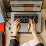 Why Wage and Payroll Compliance Is Becoming a Bigger Challenge for Employers 8 Top view of hands typing on laptop at a desk with folders and calculator