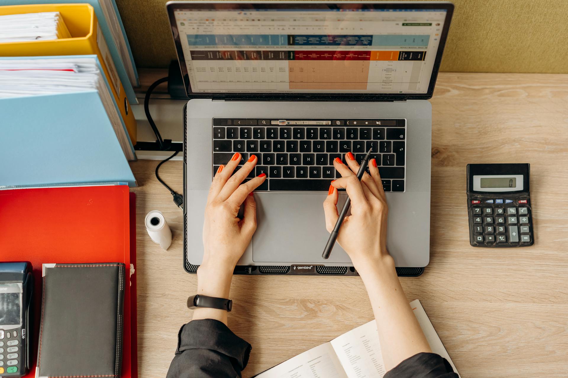 Top view of hands typing on laptop at a desk with folders and calculator