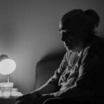 Can Family Members Be Held Responsible for Elder Neglect? 12 A contemplative senior woman sits by a lamp in a dimly lit room, evoking deep thought and solitude