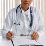 A focused doctor with stethoscope recording patient details in an office setting