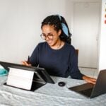 A young woman smiling while working on a laptop and drawing tablet at home