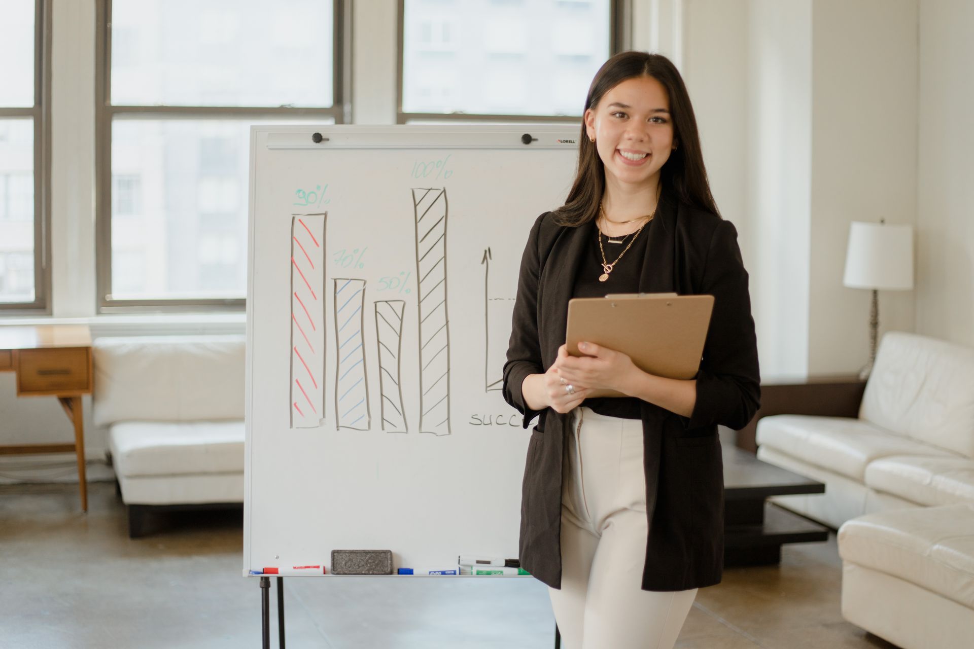 Confident businesswoman presenting charts and data analysis on a whiteboard in a modern office setting