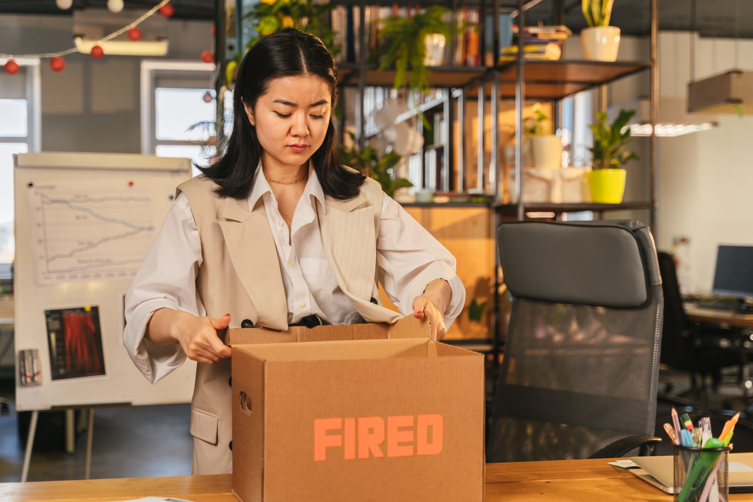 An Asian woman packs a box labeled 'FIRED'