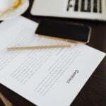 Close-up of a contract with office essentials like a laptop and coffee on a desk