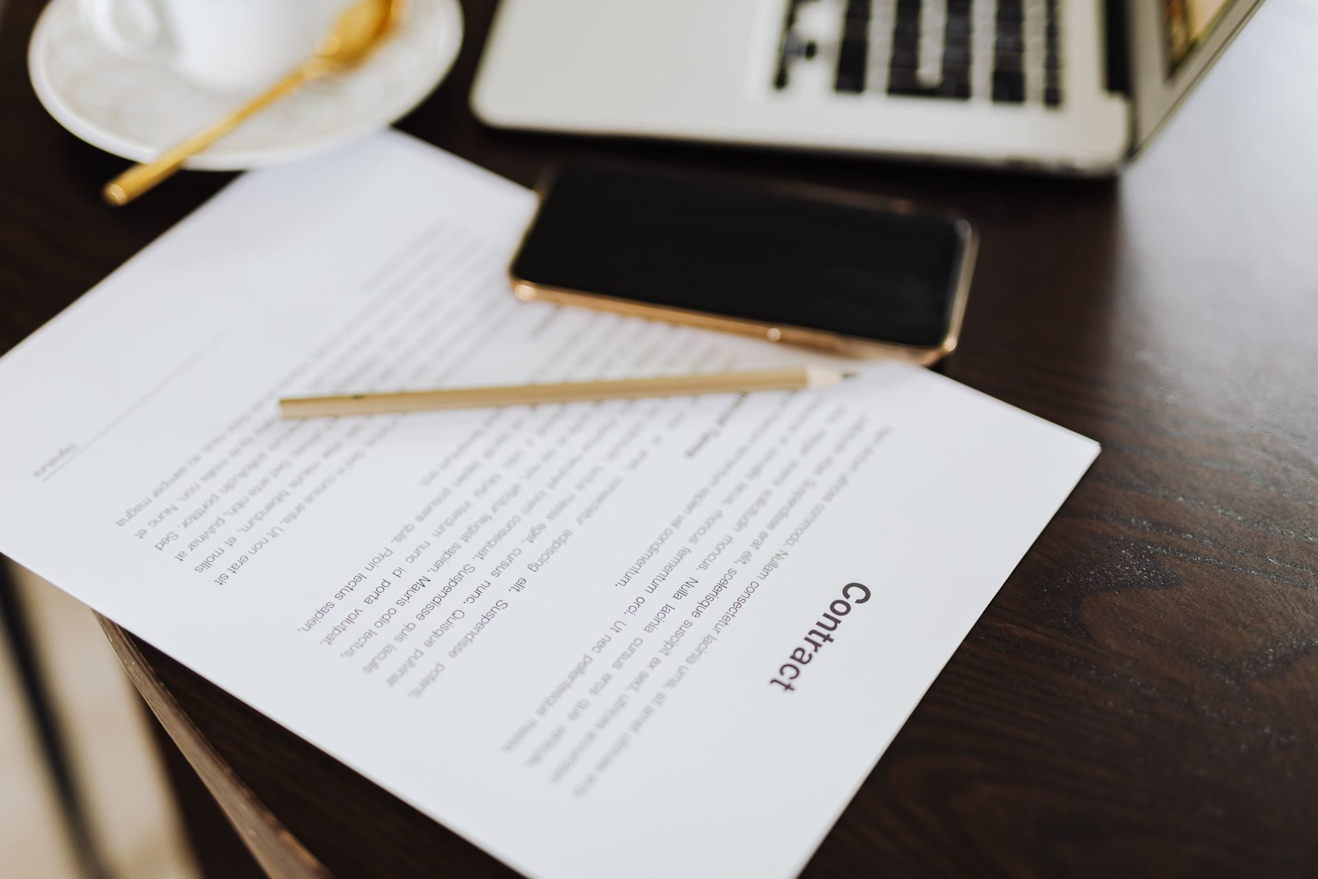 Close-up of a contract with office essentials like a laptop and coffee on a desk