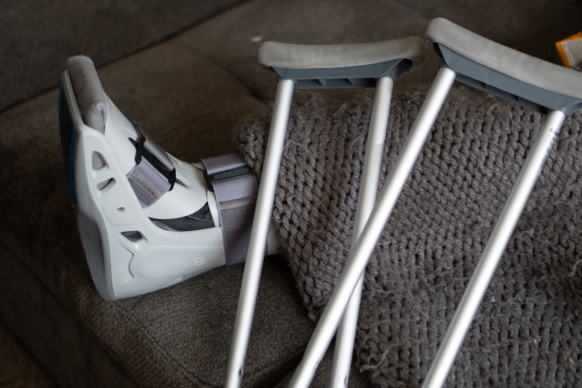 Close-up of an orthopedic boot and crutches on a couch, symbolizing injury recovery at home