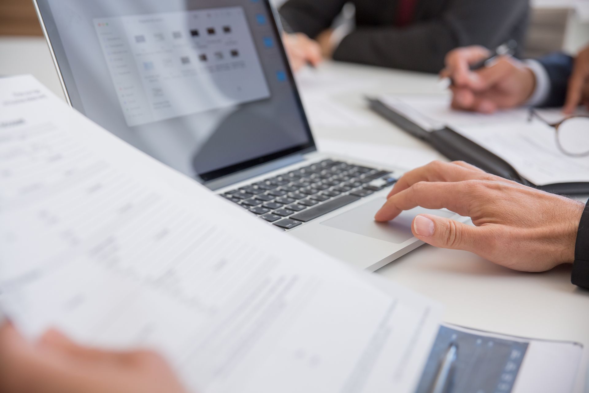 Close-up of hands working on documents and a laptop in an office setting, illustrating teamwork and productivity