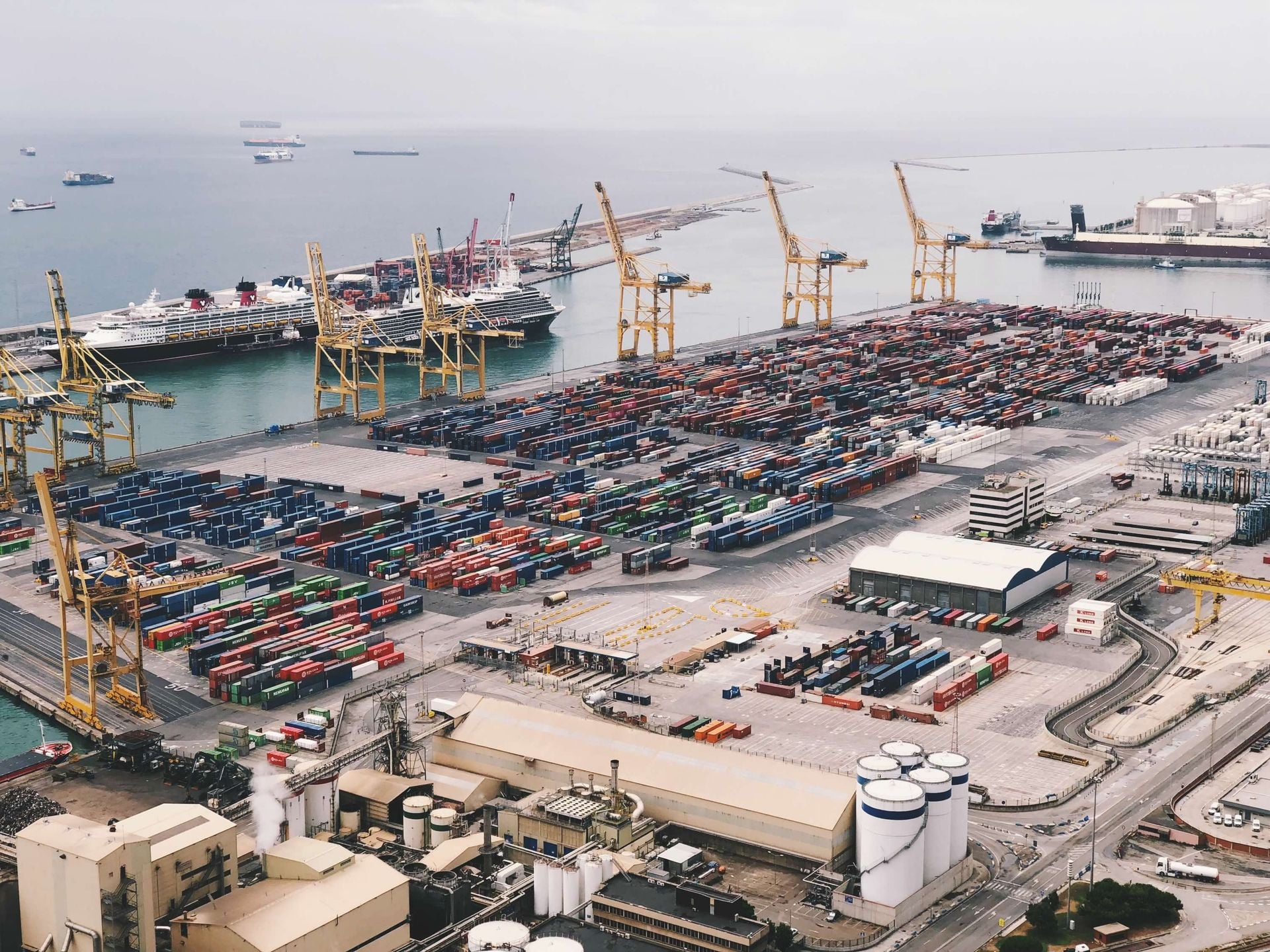 Expansive aerial view of a bustling container port with large cranes and cargo ships under a cloudy sky