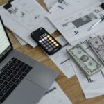 7 Best Payroll Audit Software Tools for 2026 7 A desk with financial documents, currency, a laptop, and phone calculator.