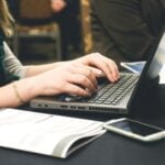 Cloud PDF Tools to Merge Documents on Clinic Computers Without Installing Anything 10 Adult woman typing on a laptop at a desk with a smartphone and documents